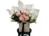 A close up image of a soft pastel blush pink, cream and jasmine flower bouquet, wrapped in signature Kate Hill style and sitting on a black bentwood chair in front of white wall.