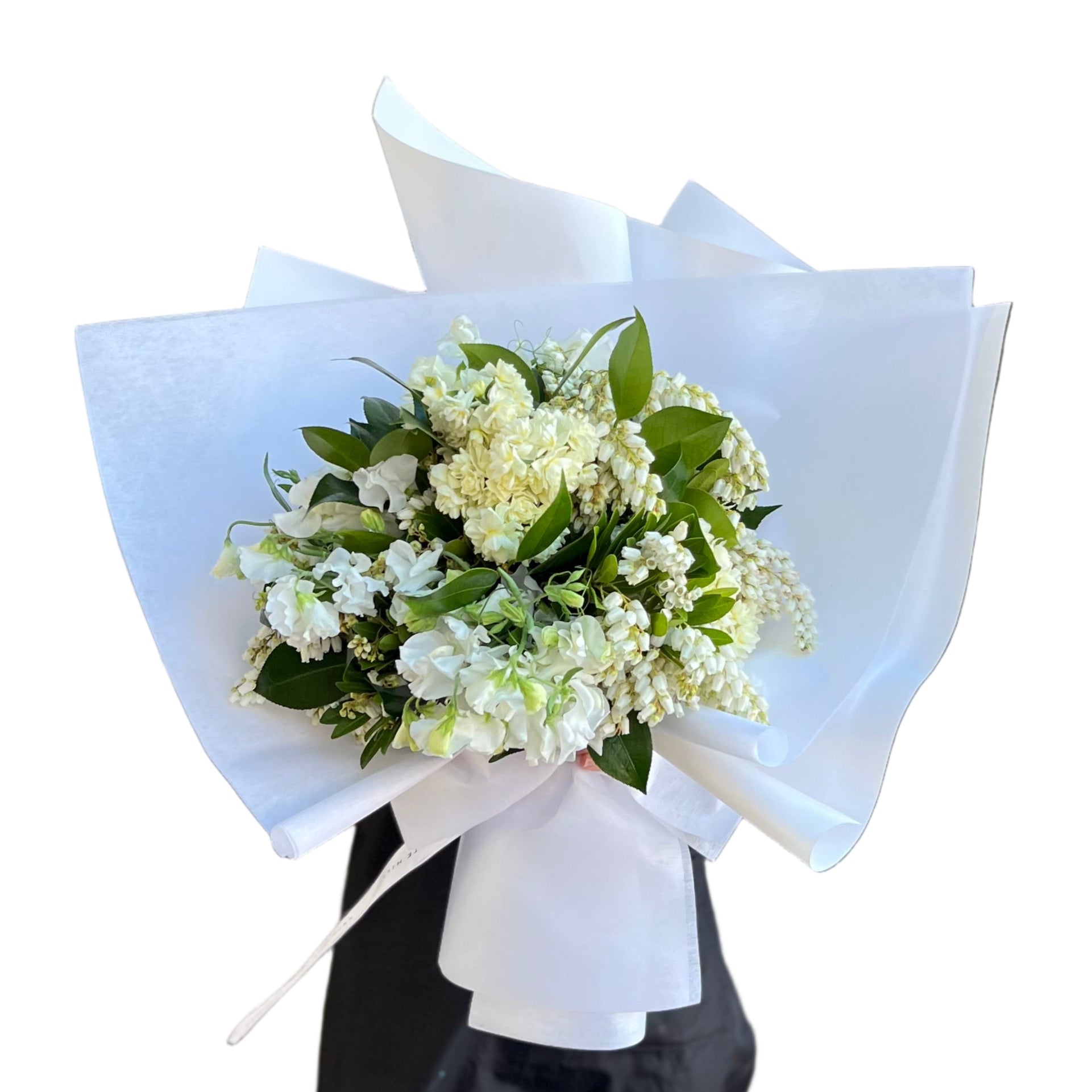 Florist holding a Bouquet of white, cream and lemon Spring flowers in a white Kate Hill Flowers bag, sitting on  black bentwood chair against a white wall.