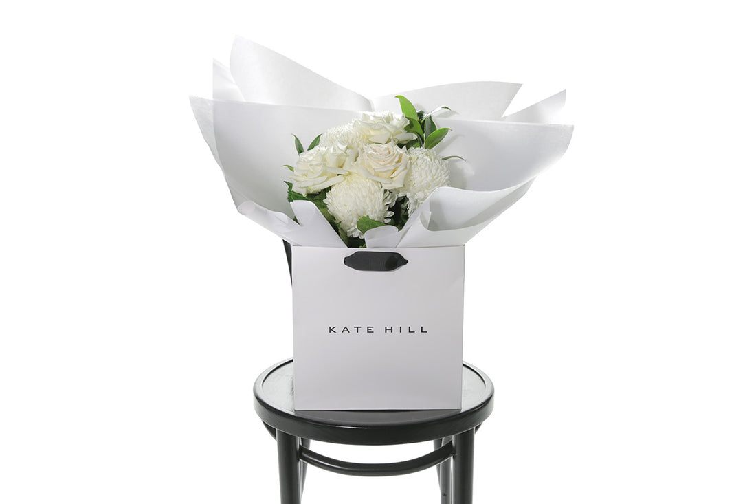 Kate Hill Flowers – small white sympathy posy of roses and chrysanthemums in a water-filled gift bag.