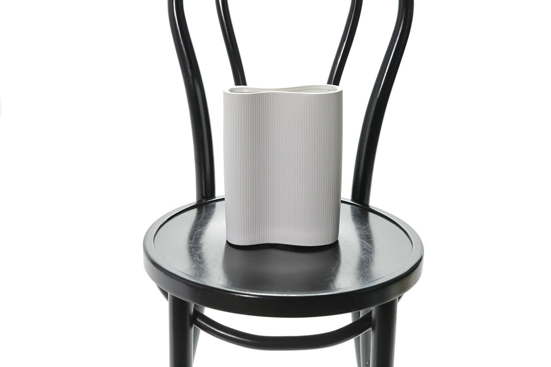 Close up image of white ceramic vase. A 22cm White ceramic wave vase sitting on black bentwood chair with white background.