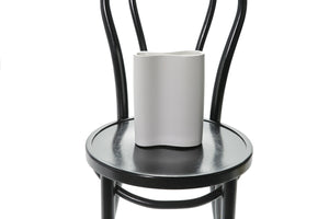 Close up image of white ceramic vase. A 22cm White ceramic wave vase sitting on black bentwood chair with white background. 