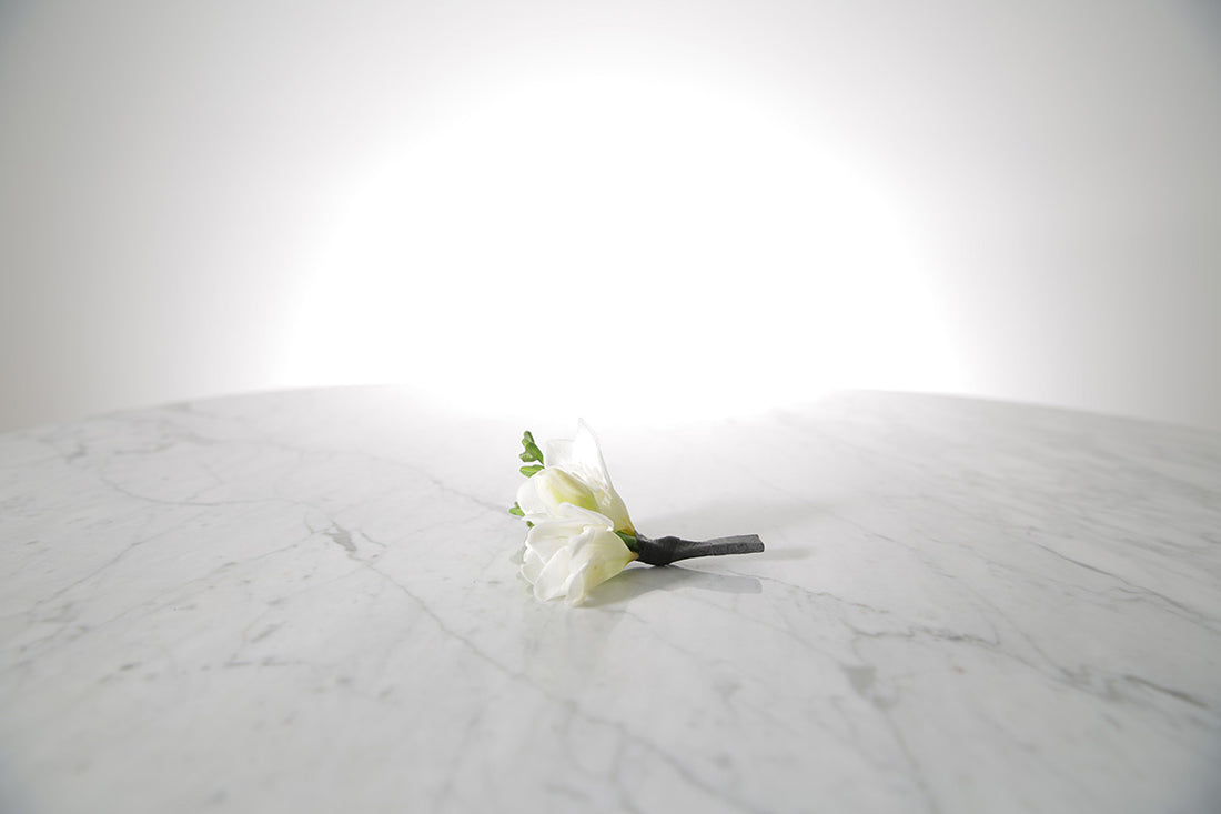 Single white freesia buttonhole flower on a marble surface with a light grey background