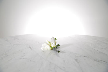 White floral freesia buttonhole on a marble surface with a light grey background