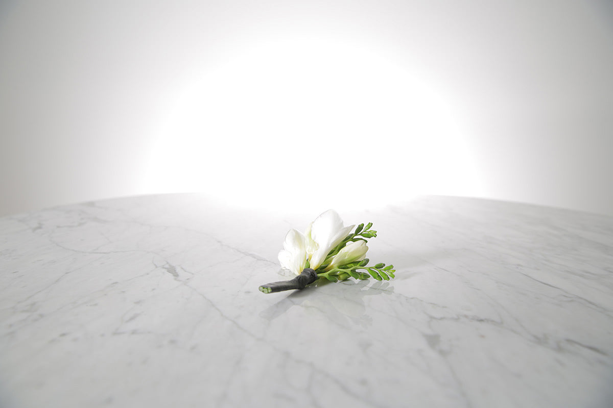 White freesia buttonhole flower on a marble surface with a light grey background