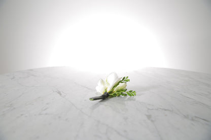 White freesia buttonhole flower on a marble surface with a light grey background