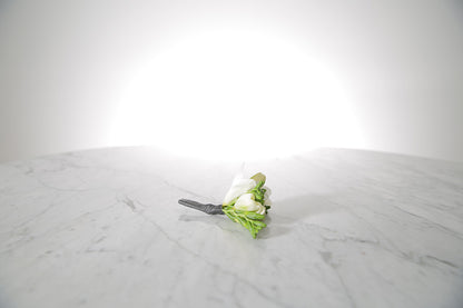 White freesia buttonhole flowers with a black holder on a marble surface