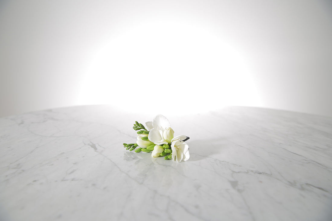 White buttonhole flowers on a marble surface with a light grey background