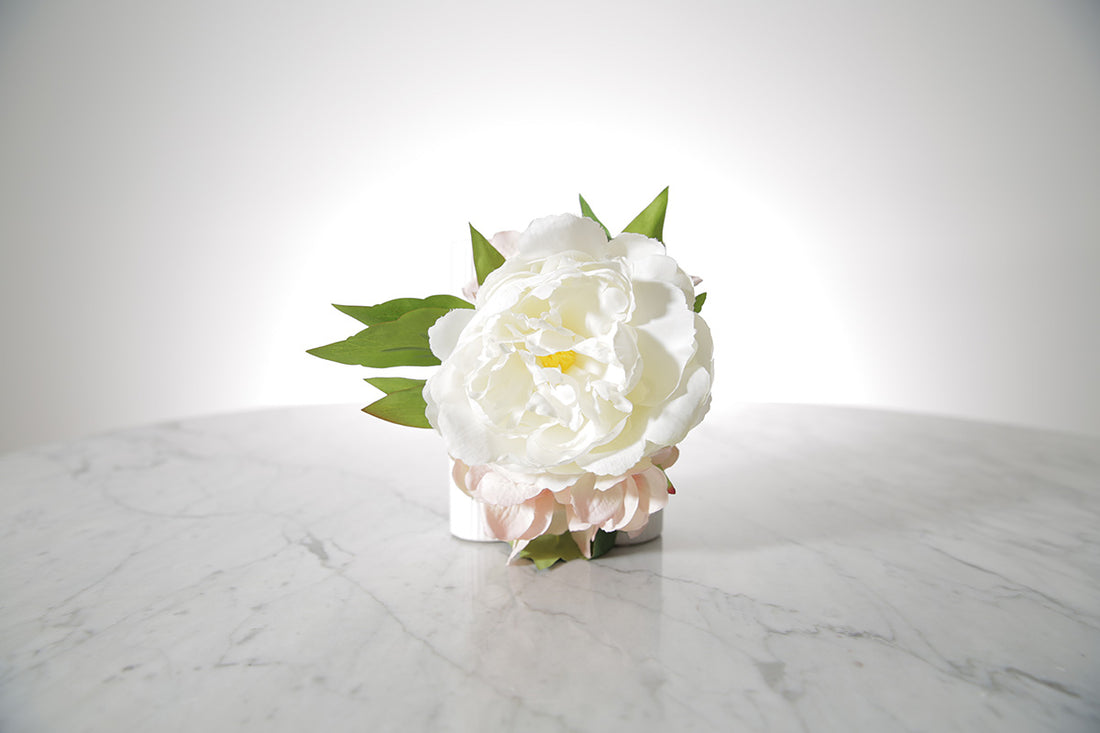 Kate Hill Flowers artificial white peony and blush hydrangea wrist corsage on silver elastic wristlet, displayed on a marble table with a white background.