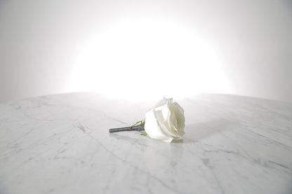Kate Hill Flowers white rose buttonhole flower with black-taped stem and pearl pin, lapel-ready on a marble surface with a light grey background.