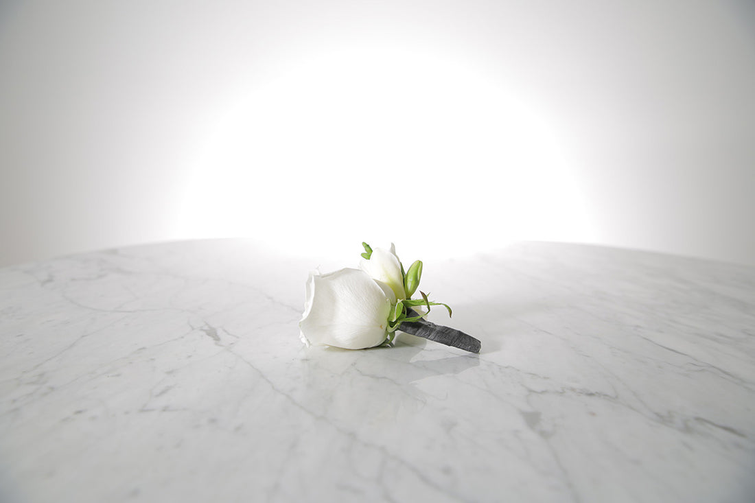 White rose and freesia buttonhole with black-taped stem and pearl pin with a light grey background