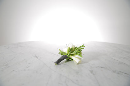 White rose and freesia buttonhole with black-taped stem and pearl pin with a light grey background