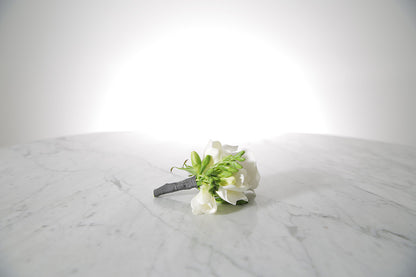 White rose and freesia buttonhole with black-taped stem and pearl pin with a light grey background