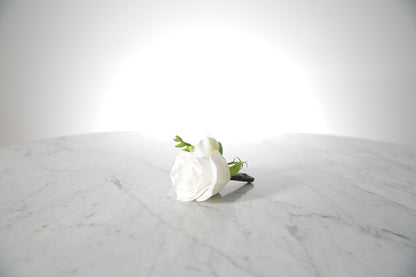 white rose and freesia buttonhole with black-taped stem and pearl pin with a light grey background