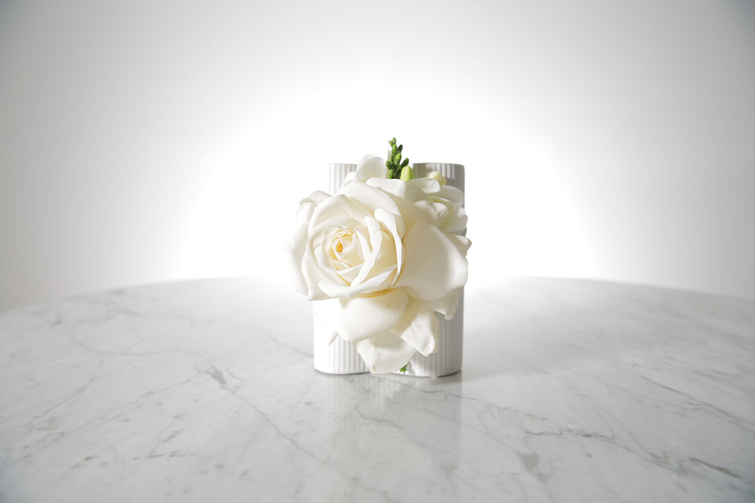Kate Hill Flowers white rose and freesia wrist corsage on a silver elastic wristlet, boxed and ready to wear. Displayed on a marble table with a white background.