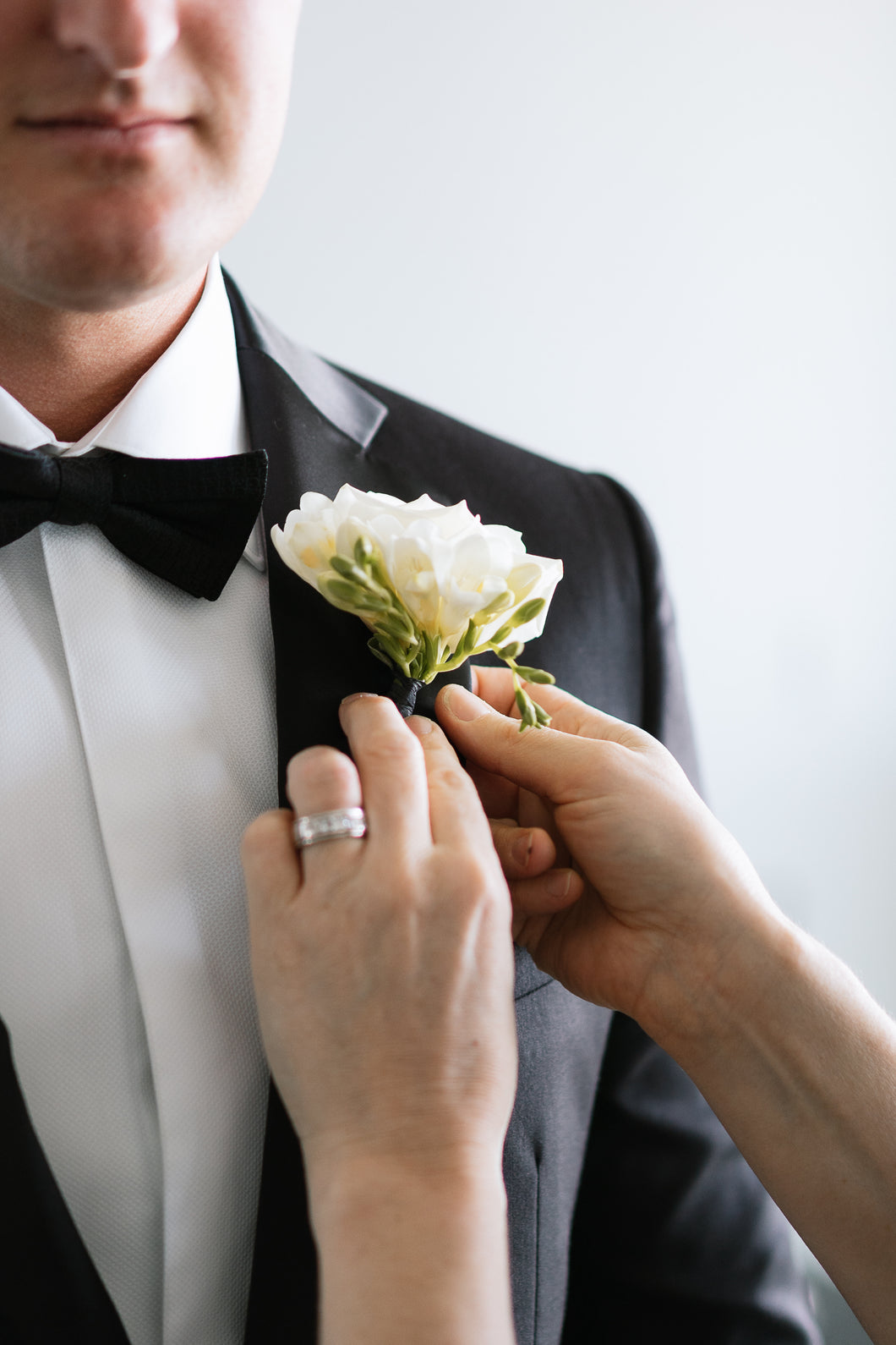 Groom being pinned by Kate hill the florist with a buttonhole. Black tie jacket suite lapel with white freesia buttonhole.