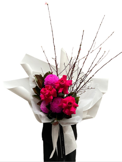 A Melbourne florist wearing black holding a bouquet of flowers with hot pink flowers wrapped in white paper against a white wall.