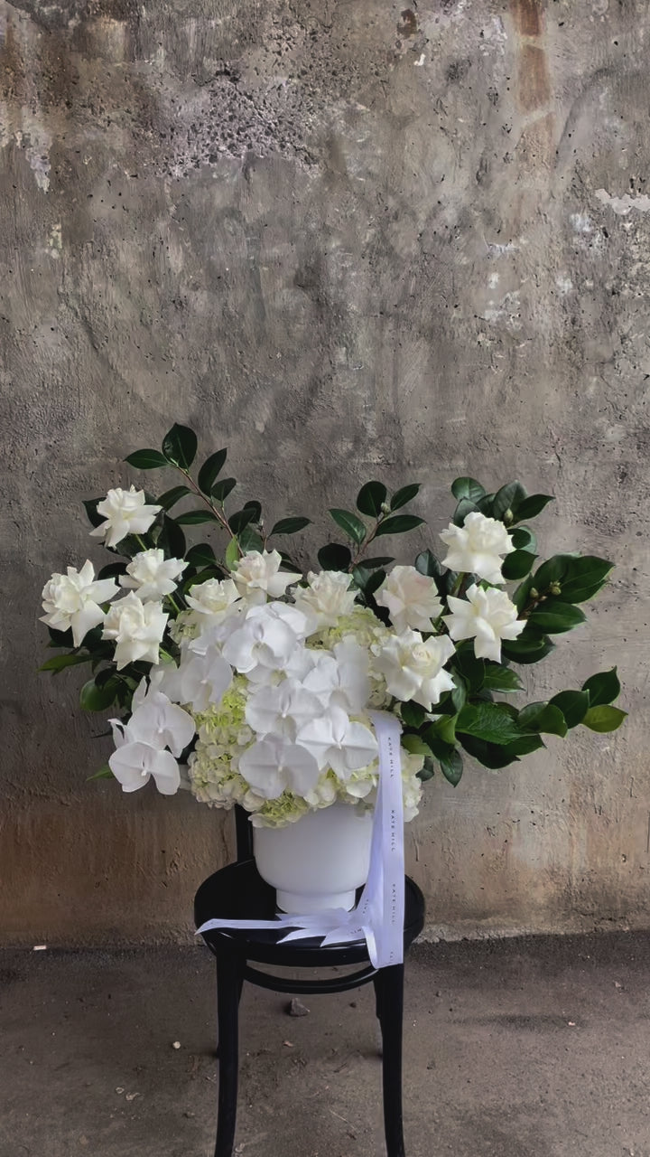 Video of a large luxe white flower design sitting on a black bentwood chair with concrete wall behind.