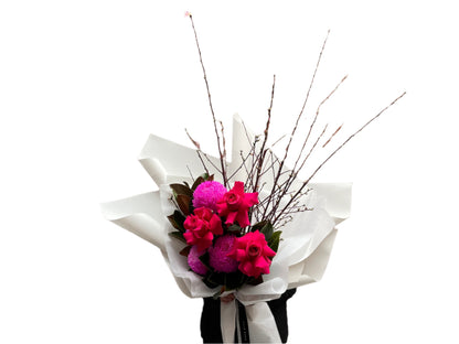 A Melbourne florist wearing black holding a bouquet of flowers with hot pink flowers wrapped in white paper against a white wall.