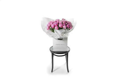 Best selling Peony Rose bouquet featuring 15 stems of pink peonies (flower only). Bouquet of peony roses presented in white signature wrapping and placed into Kate Hill Flower Bag. Wide image of the Peony Rose bouquet.
