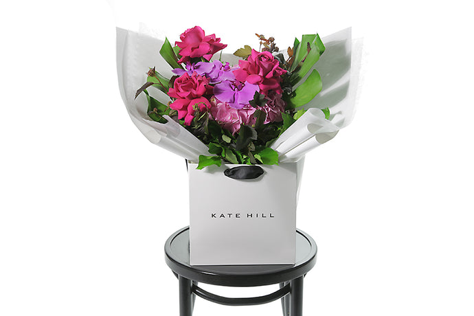 A bright pink, magenta and soft pink gift bouquet named ARIA beautifully gift wrapped in our Kate Hill signature wrapping. Gift bouquet is presented into our Kate Hill flower bag to ensure the bouquet remains fresh in water. ARIA bouquet is sitting on a black bentwood chair.