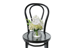 Petite ribbed glass vase displaying white and green seasonal flower. Gift includes the vase. BAILEY vase flower design is beautifully presented in our flower bag and detailed with Kate Hill ribbon. Small vase design is sitting on black bentwood chair.