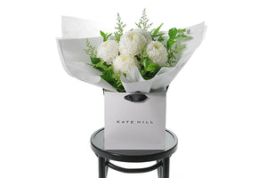 FLORENCE is a hand tied bouquet crafted with 5 stems of white Disbuds and green seasonal foliages which are beautifully gift wrapped in our signature wrapping. Bouquet is placed into a Kate Hill flower bag. Flower flower bag is sitting on a black bentwood chair.