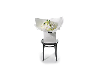 Small chic bouquet displaying a dome of white hydrangeas (no additional foliage). Bouquet presented in Kate Hill Flower Bag. Wide image of the Freya Hydrangea Flower Bouquet.