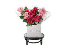 A large bouquet of mixed reflexed bright roses with lush green foliages. Beautifully wrapped in signature Kate Hill Flowers wrapping and placed into flower bag. Bouquet bag sitting on a black bentwood chair.