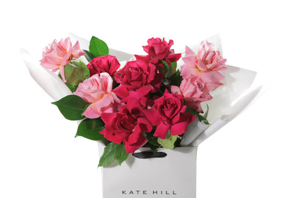 Close up image of the GEORGIA Rose Bouquet so you can see the reflexed roses and the quality. A large bouquet of mixed reflexed bright roses with lush green foliages. Beautifully wrapped in signature Kate Hill Flowers wrapping and placed into flower bag. Bouquet bag sitting on a black bentwood chair.