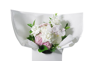 Pastel pink and white flower bouquet with seasonal foliage. Gift Bouquet presented in Kate Hill Flower Bag. Medium sized bouquet sitting on a black bentwood chair with white background. Close up image of the Serenity Flower Bouquet.