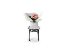 Wide image of the VERA rose flower bouquet. VERA is classed as a small sized, hand tied bouquet of 10 stems of Classic Roses (no additional foliage with roses only).  Vera rose bouquet is beautifully wrapped in our signature wrapping and placed into our flower bag. Bouquet bag is sitting on a black bentwood chair.