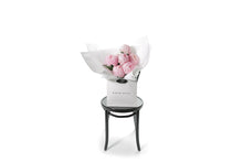 Wide image of the pink disbud bouquet. Pink Big Mom Disbud Gift Bouquet displaying 10 stems of pink Disbuds (no additional foliage) flower only. Gift Bouquet presented in Kate Hill Flower Bag. Bouquet bag sitting on a black bentwood chair.