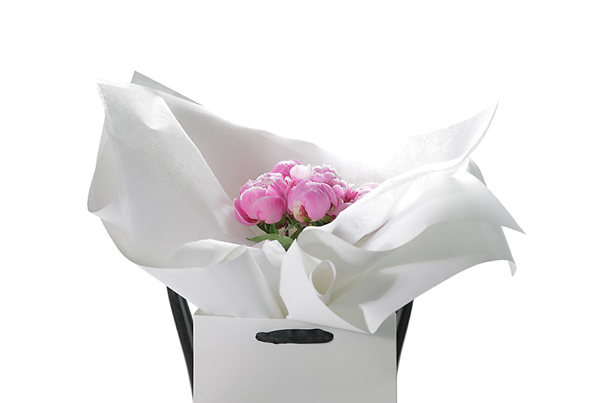 Close up image of the ZOEY peony rose bouquet. 5 Stems of seasonal pink peony roses gift wrapped beautifully in signature white wrapping. Bouquet presented in Kate Hill Flower Bag. Bouquet bag sitting on a black bentwood chair.